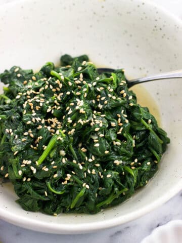 A serving dish of sauteed spinach with a spoon