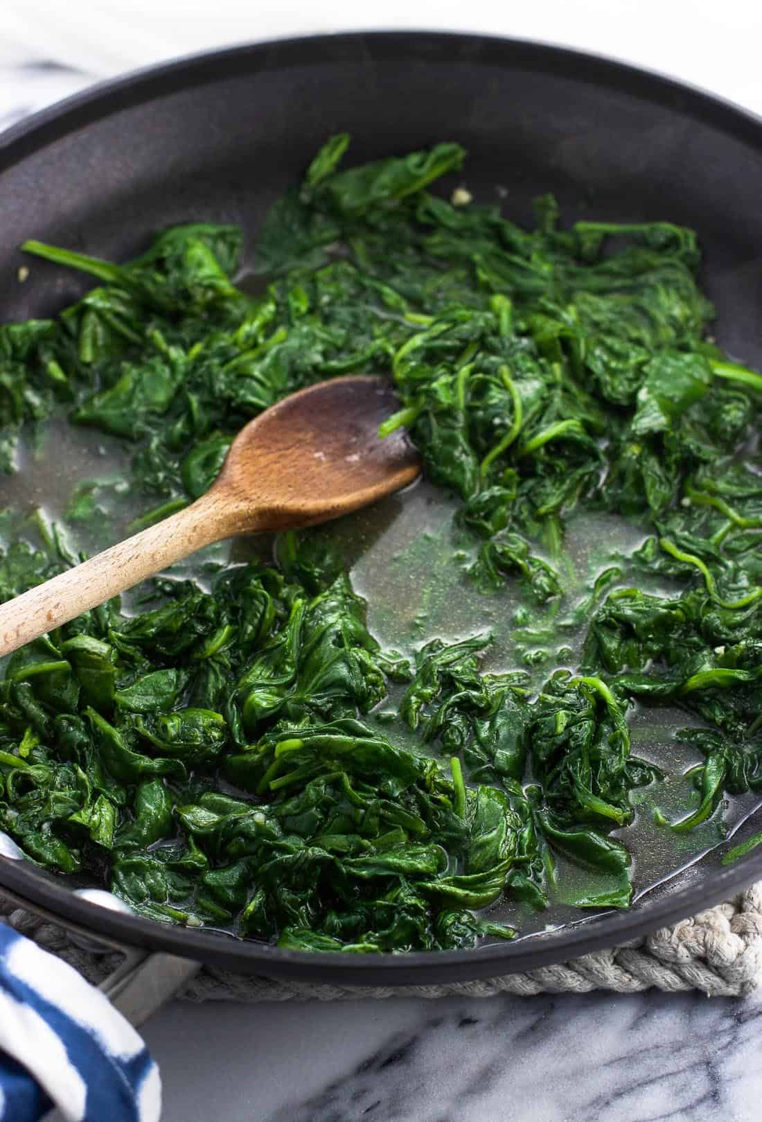 Spinach sauteeing in a skillet with a wooden spoon
