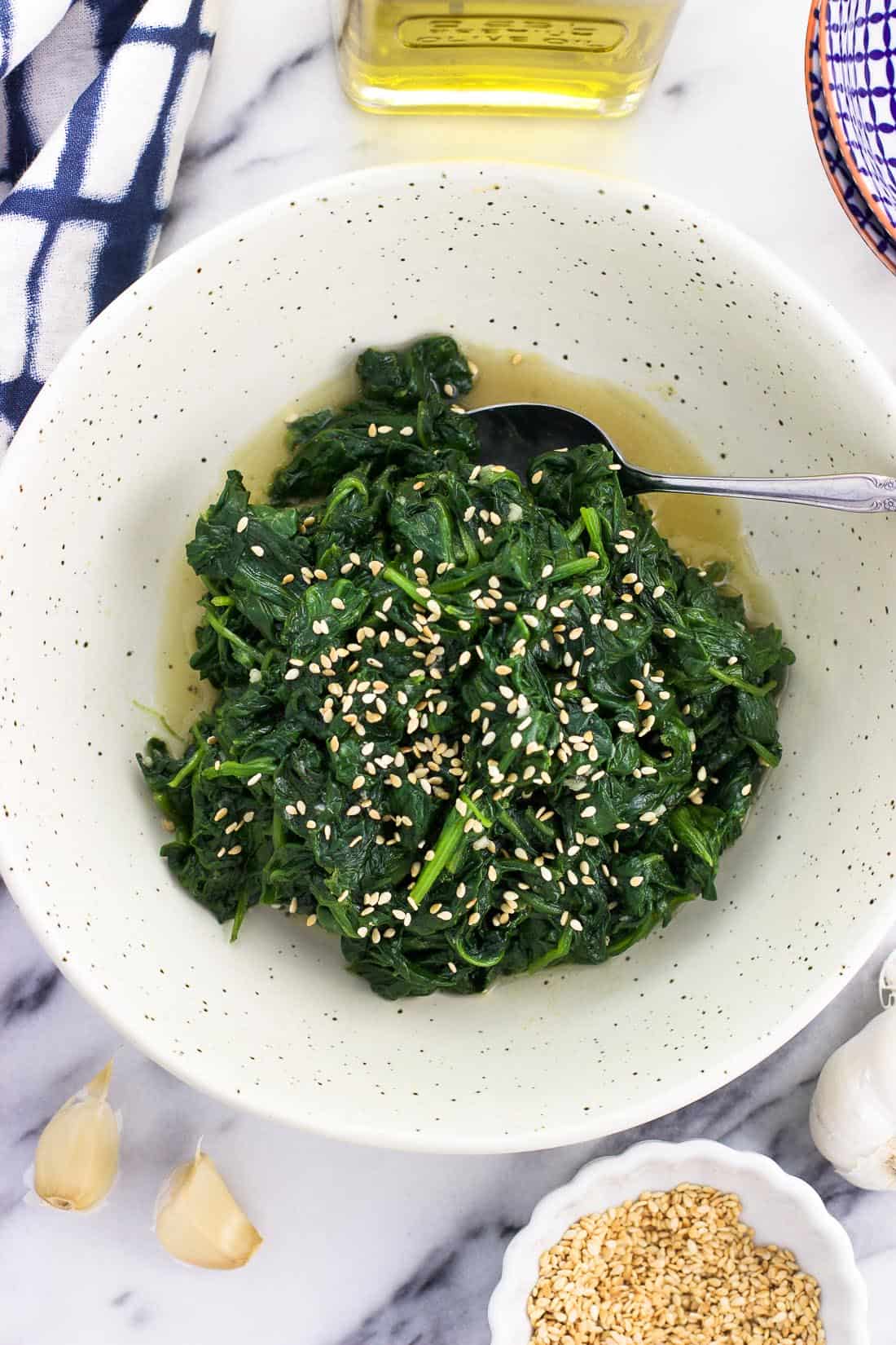 An overhead picture of sesame spinach in a serving bowl with a spoon
