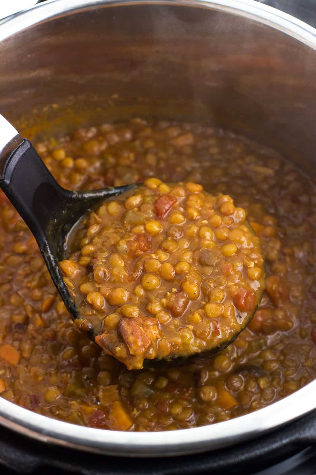 A ladle of lentil soup being lifted out of the Instant Pot after cooking.