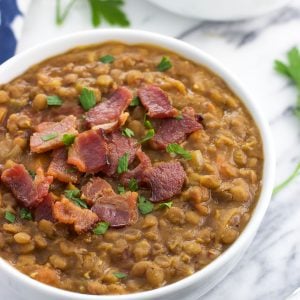 A close-up of a ceramic bowl of lentil soup topped with crumbled bacon