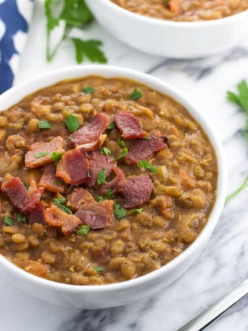 A close-up of a ceramic bowl of lentil soup topped with crumbled bacon