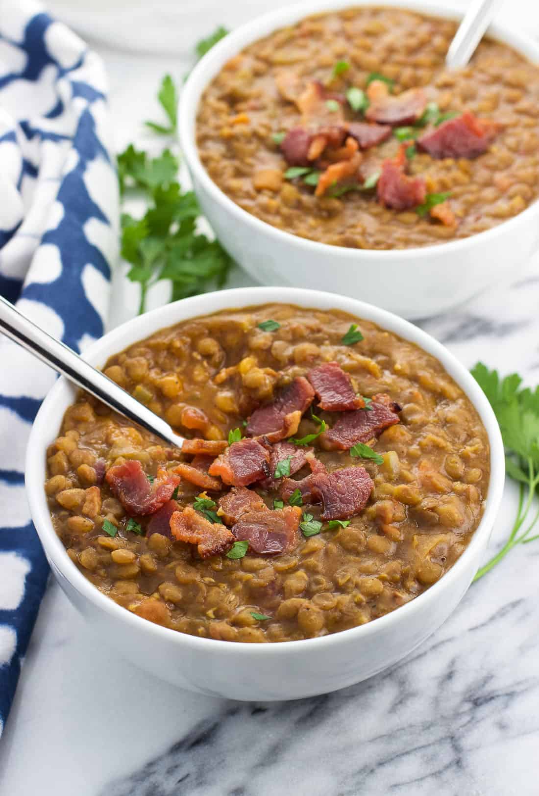 Two ceramic bowls of lentil soup topped with bacon.