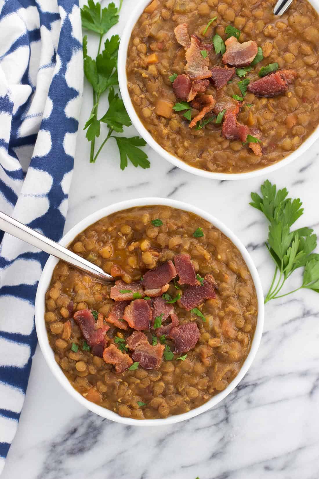 An overhead shot of two bowls of lentil soup topped with bacon with two spoons sticking out