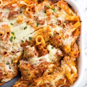 A serving spoon in a large dish of baked ziti.