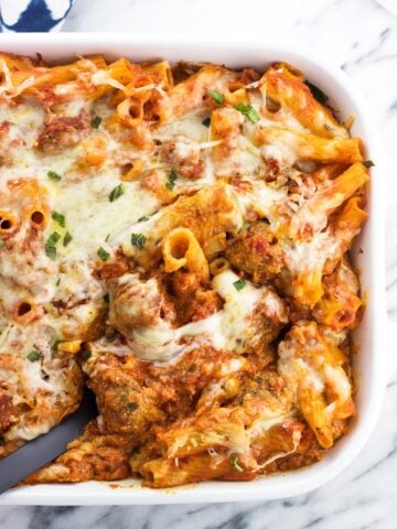 A serving spoon in a large dish of baked ziti.