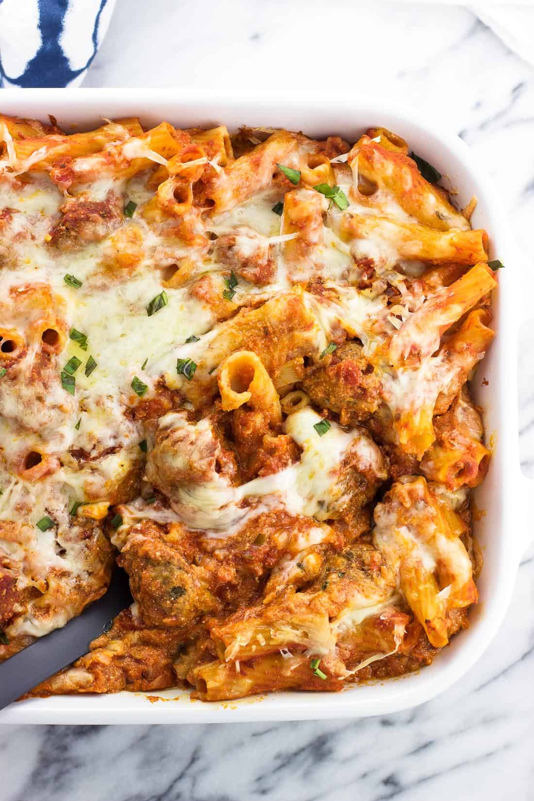 A serving spoon in a large dish of baked ziti.