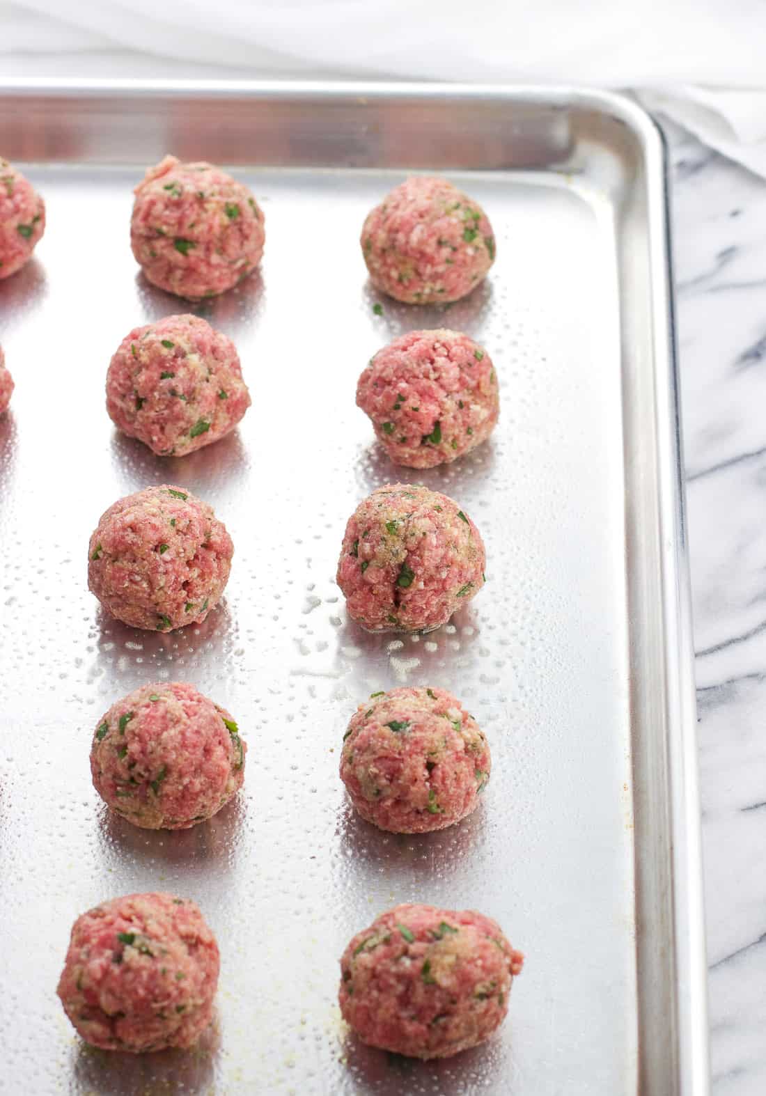 Raw meatballs lined up on an aluminum baking sheet.