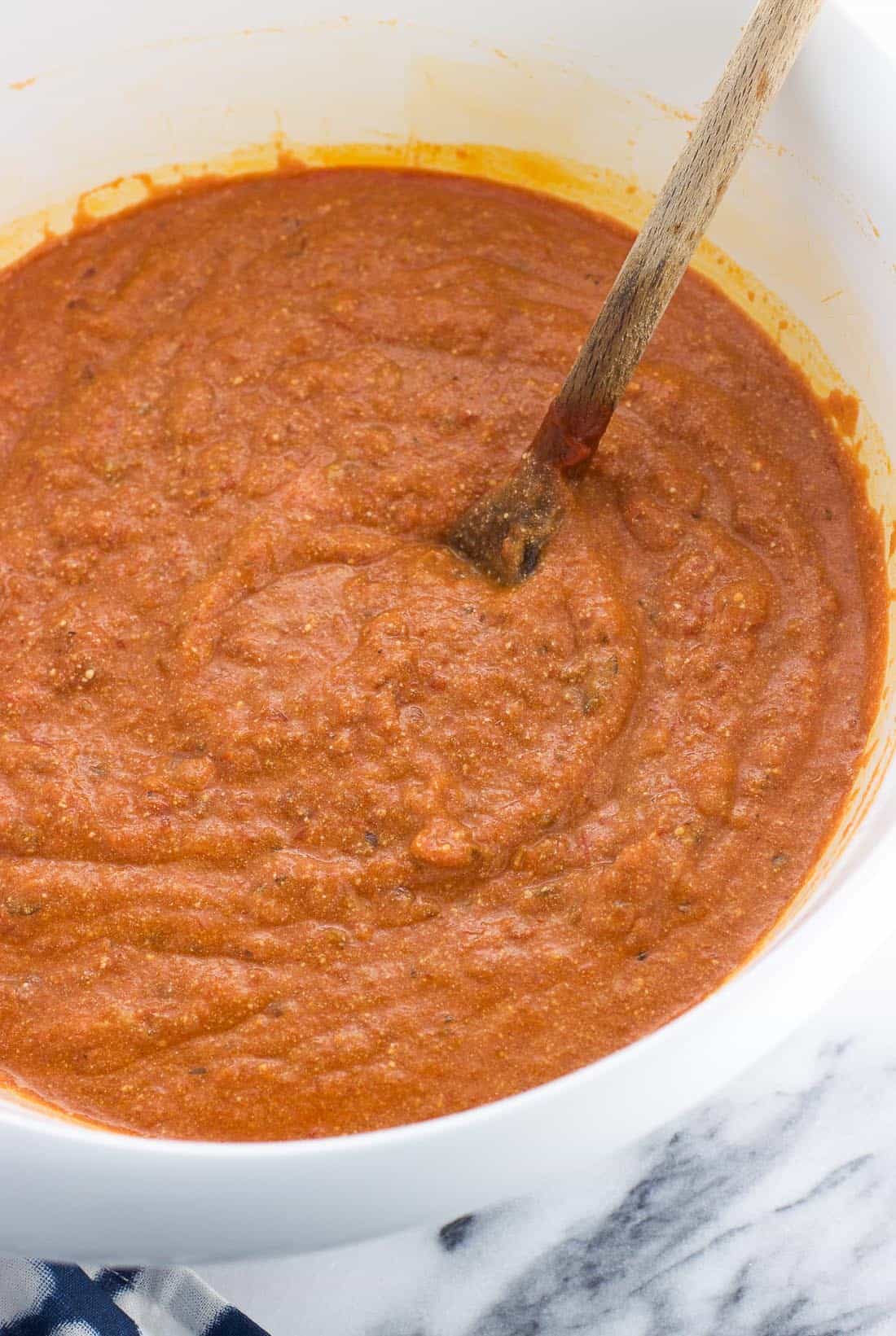 Marinara sauce and ricotta cheese mixed together in a large bowl with a wooden spoon.