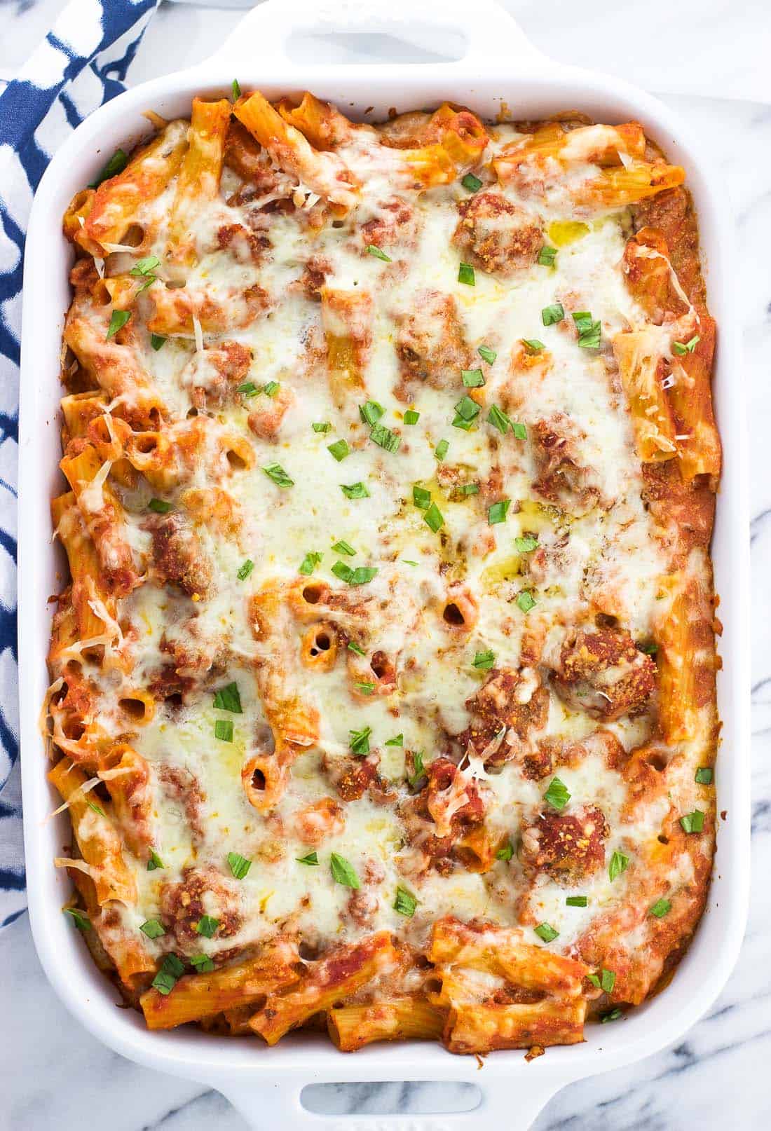 A large rectangular tray of baked ziti garnished with basil.