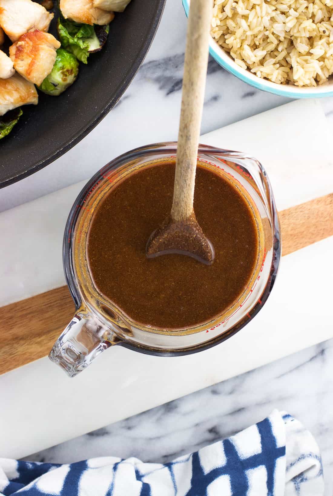 A glass measuring cup filled with balsamic peanut stir fry sauce with a wooden spoon in it.
