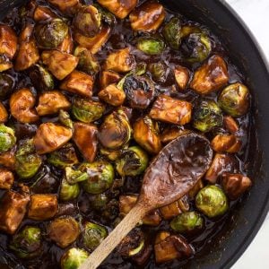 The chicken and Brussels sprouts stir fry in a skillet with a wooden spoon all ready to serve