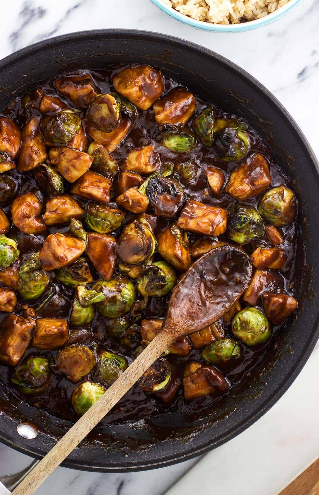 The chicken and Brussels sprouts stir fry in a skillet with a wooden spoon all ready to serve