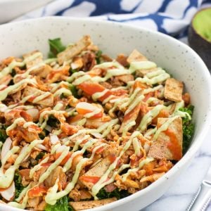 A buffalo chicken kale salad drizzled with sauce and avocado ranch dressing.