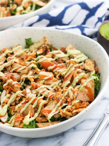 A buffalo chicken kale salad drizzled with sauce and avocado ranch dressing.