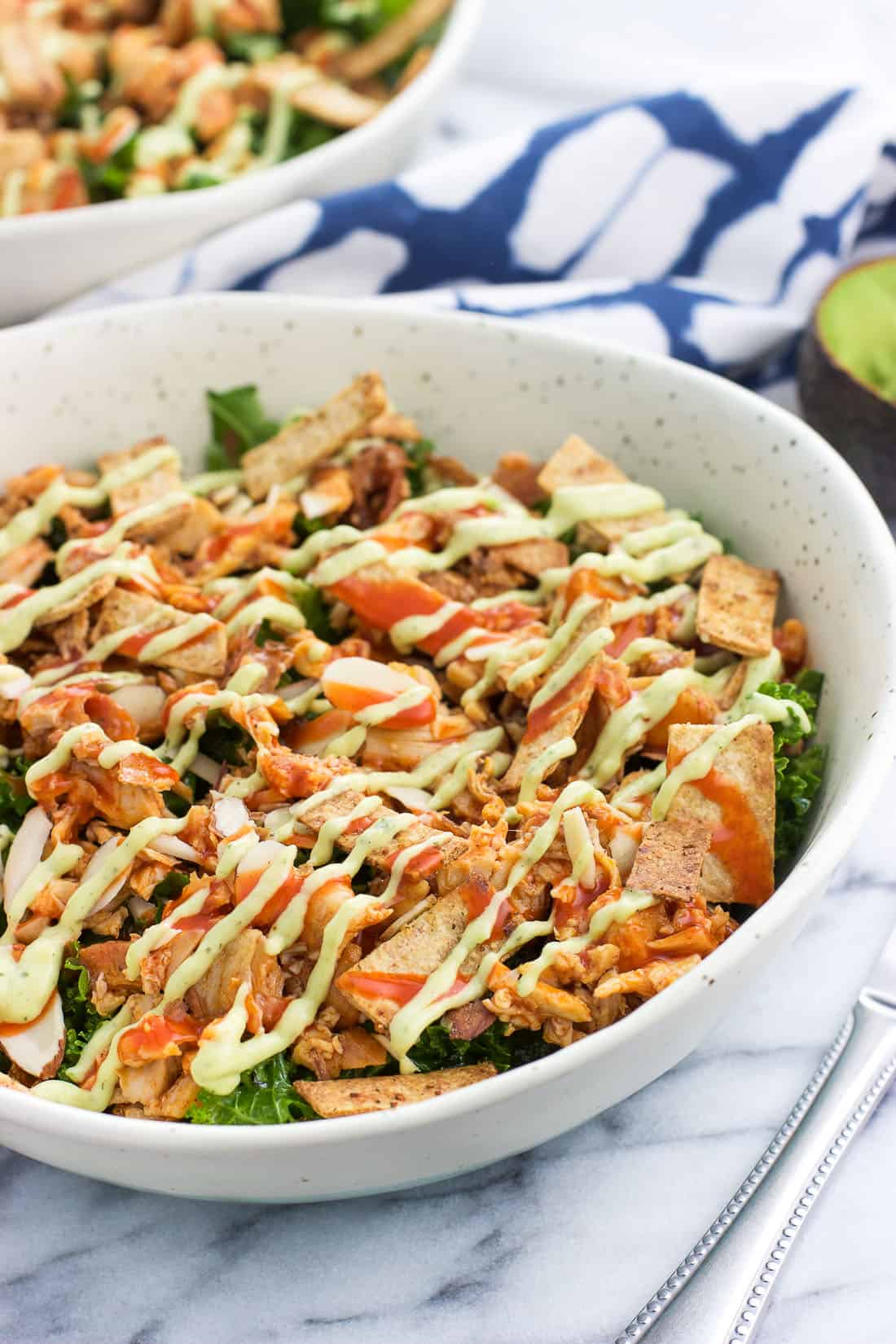 A large bowl of salad featuring buffalo chicken, tortilla strips, almonds, a buffalo sauce drizzle and avocado ranch dressing