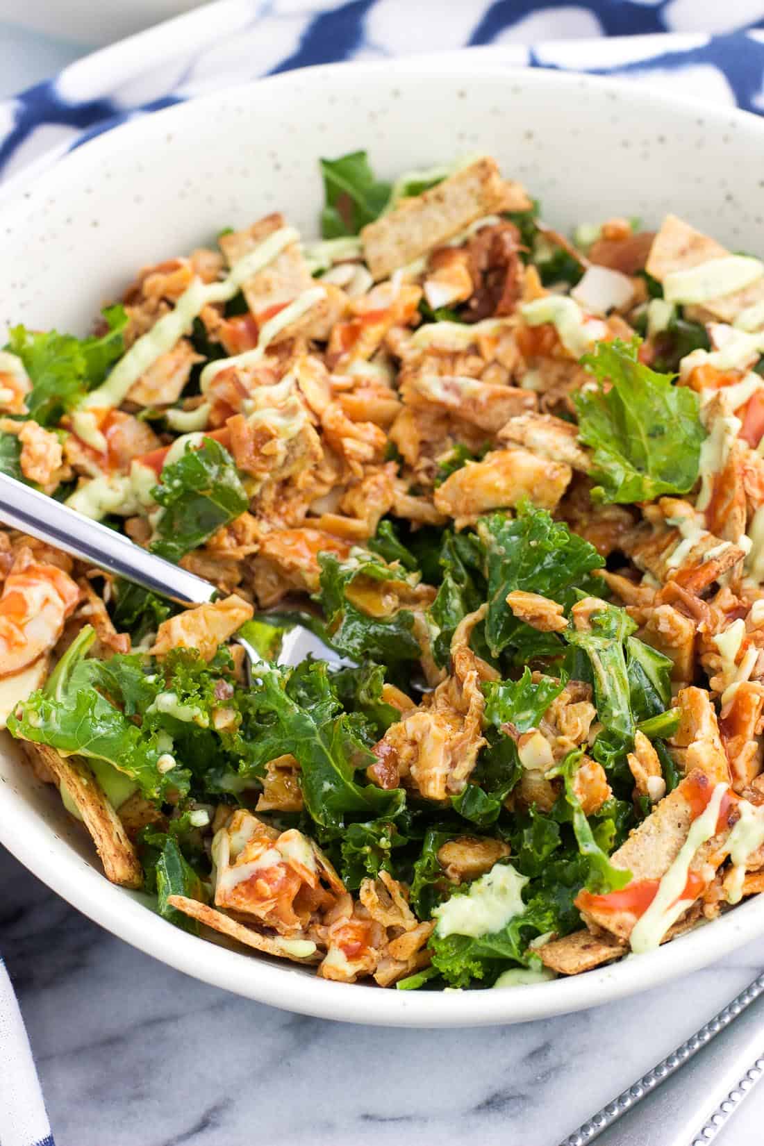 The salad in a dinner bowl all mixed together with a fork plunged into the center