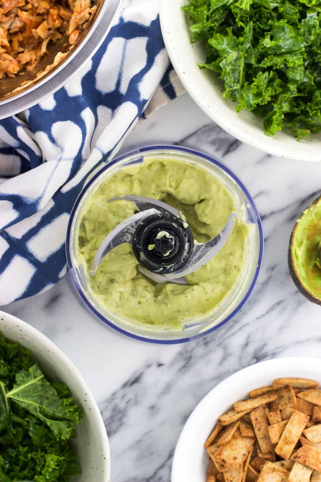 Dressing in the food processor surrounding by salad ingredients.