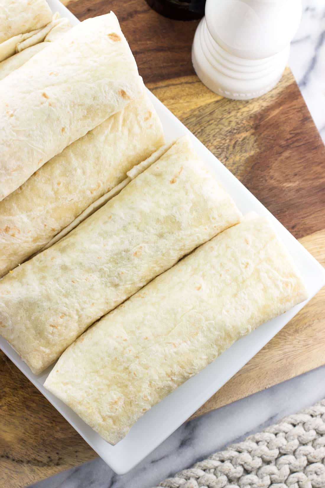 Six folded breakfast burritos on a rectangular plate.