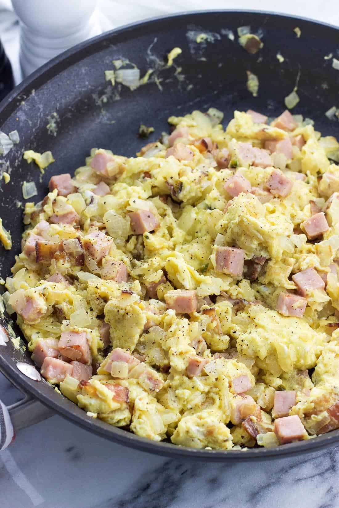 Scrambled eggs, onion, and cubed ham in a skillet.