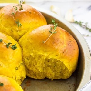 Pull-apart pumpkin rolls in a round cake pan topped with fresh thyme sprigs