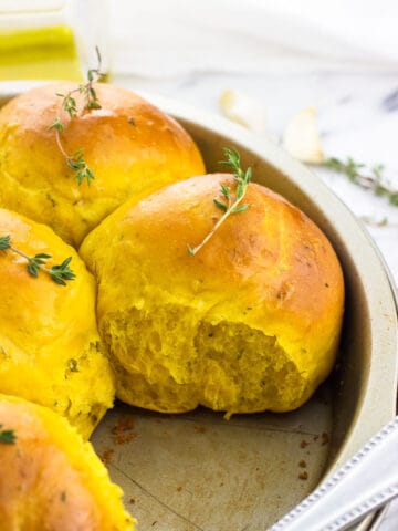 Pull-apart pumpkin rolls in a round cake pan topped with fresh thyme sprigs