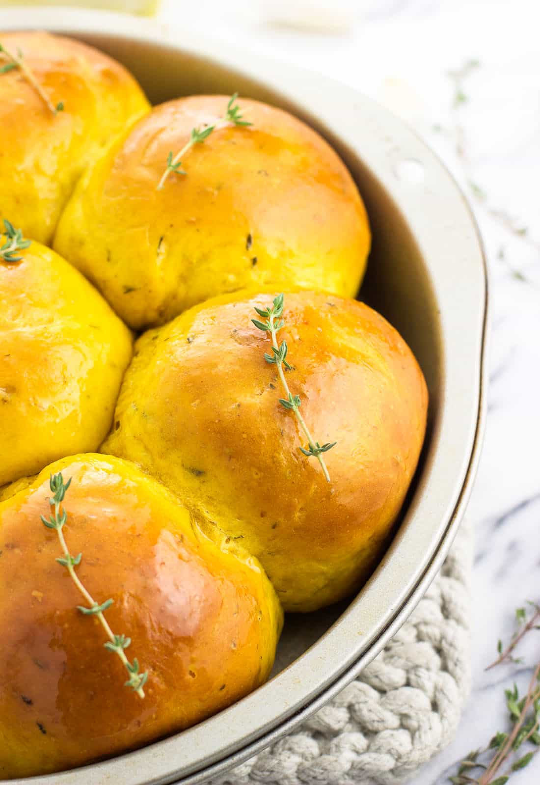A close up of the pull-apart rolls in a cake pan garnished with fresh thyme sprigs