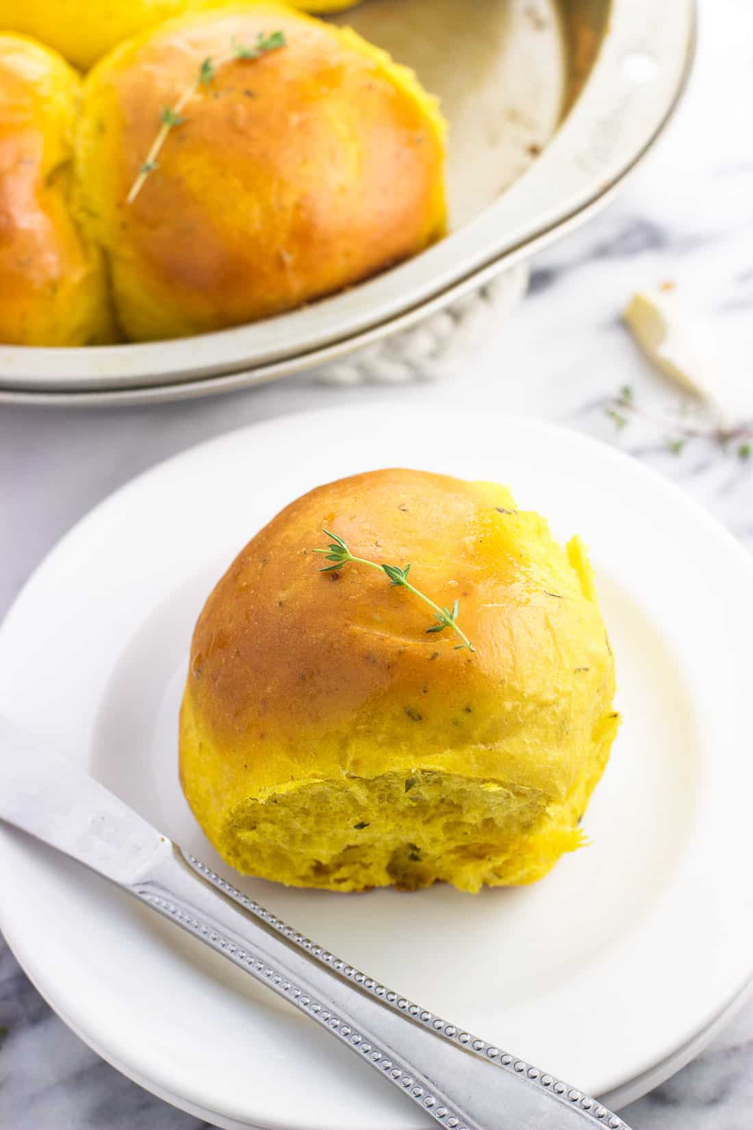 A fluffy dinner roll on a small appetizer plate next to a butter knife