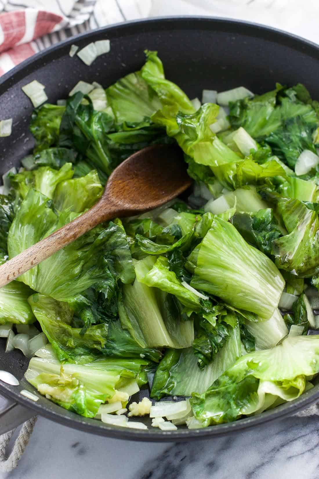 Roughly chopped escarole sautéing in a skillet with onions and garlic