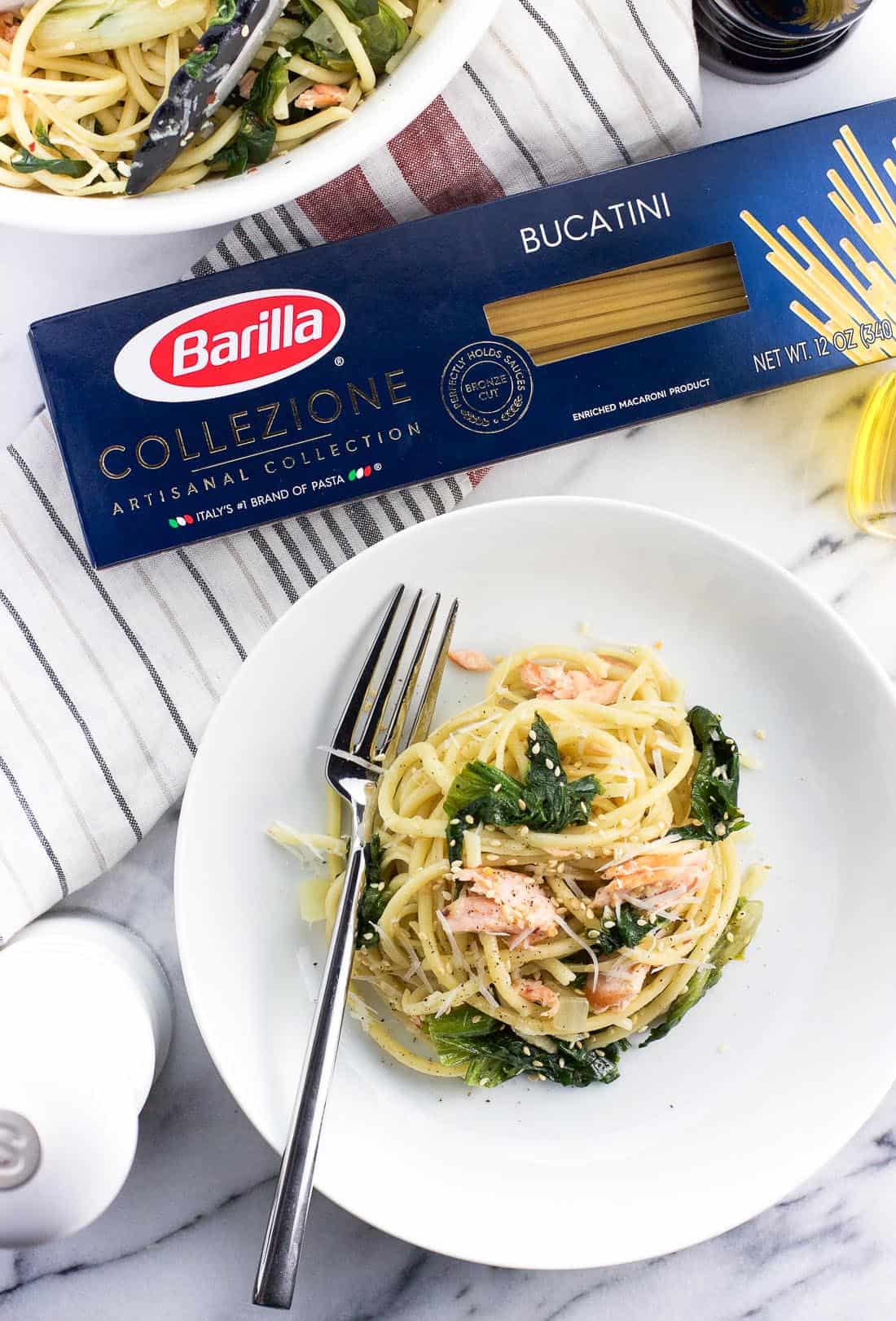 A plate of salmon pasta next to a package of Barilla Bucatini