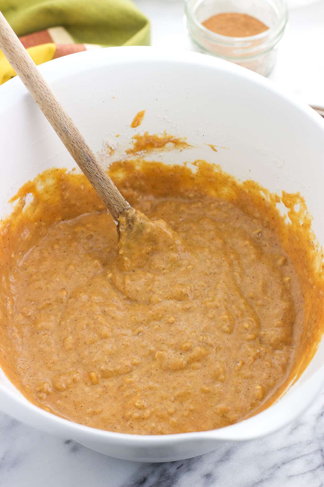 Pumpkin bread batter stirred together in a mixing bowl with a wooden spoon.