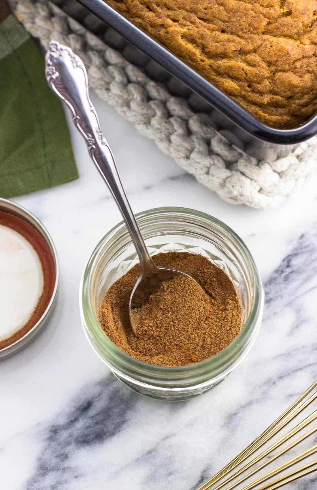 Pumpkin pie spice stirred together in a small glass jar with a spoon.