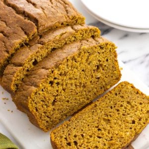 A loaf of half-sliced pumpkin bread on a serving tray.