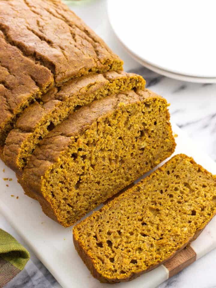 A loaf of half-sliced pumpkin bread on a serving tray.