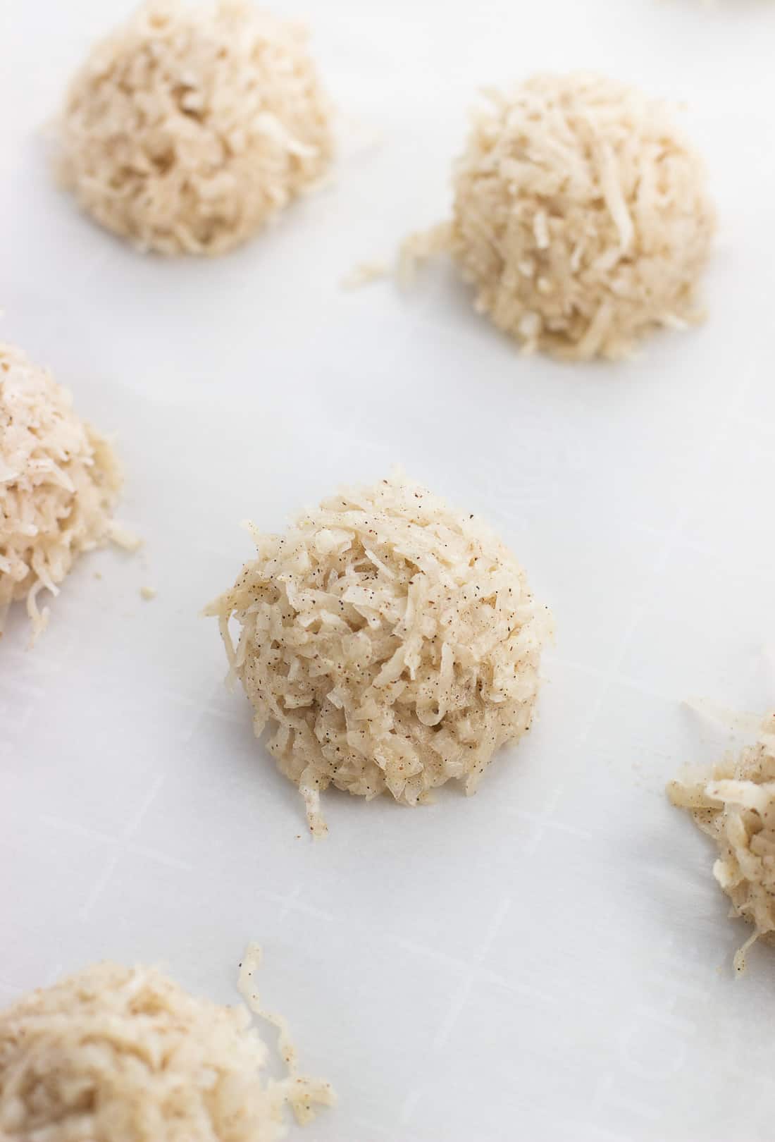 Rounded scooped coconut macaroons on a parchment-lined baking sheet before being baked.