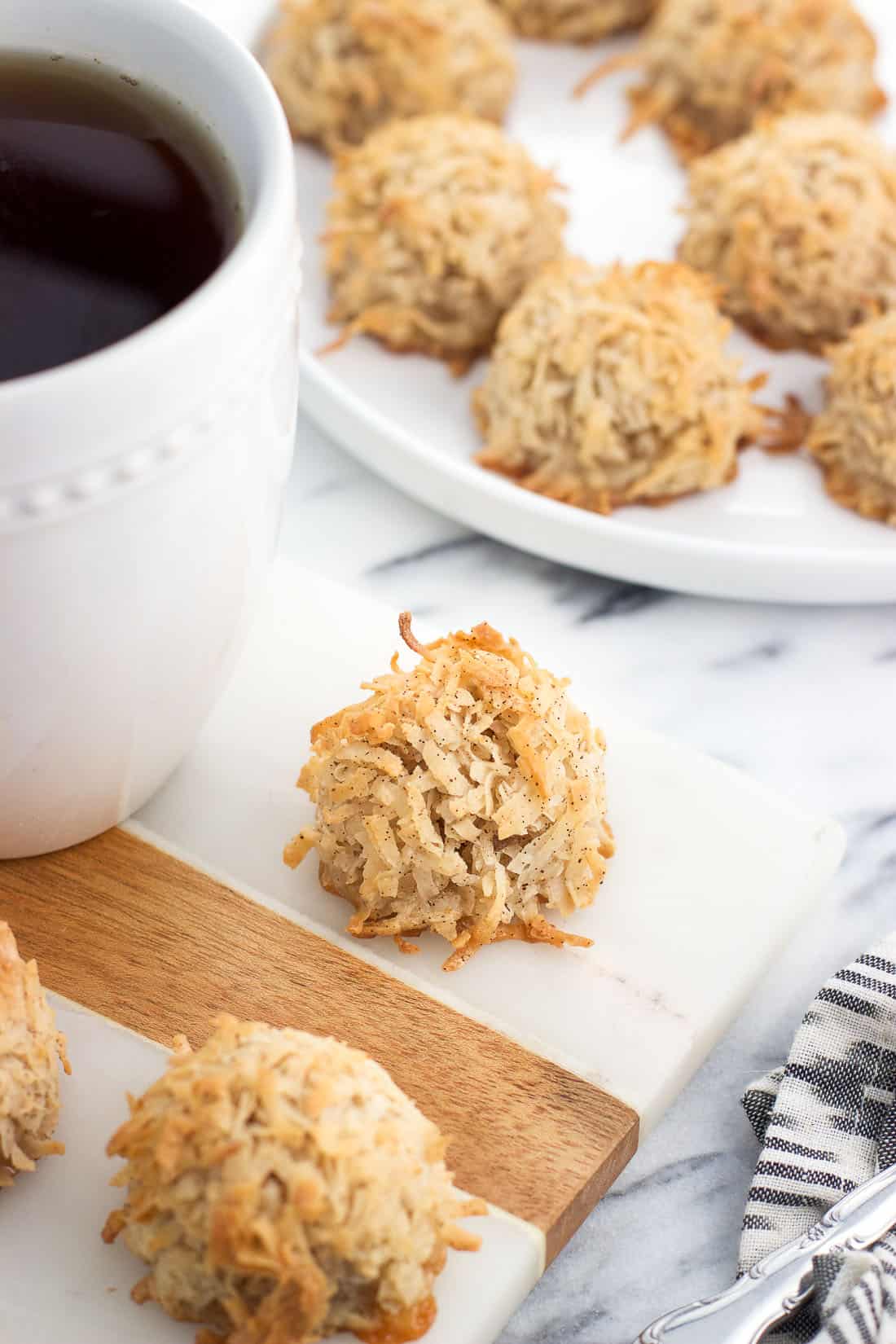 Macaroons on a marble board surrounded by more macaroons on a plate and a mug of chai tea