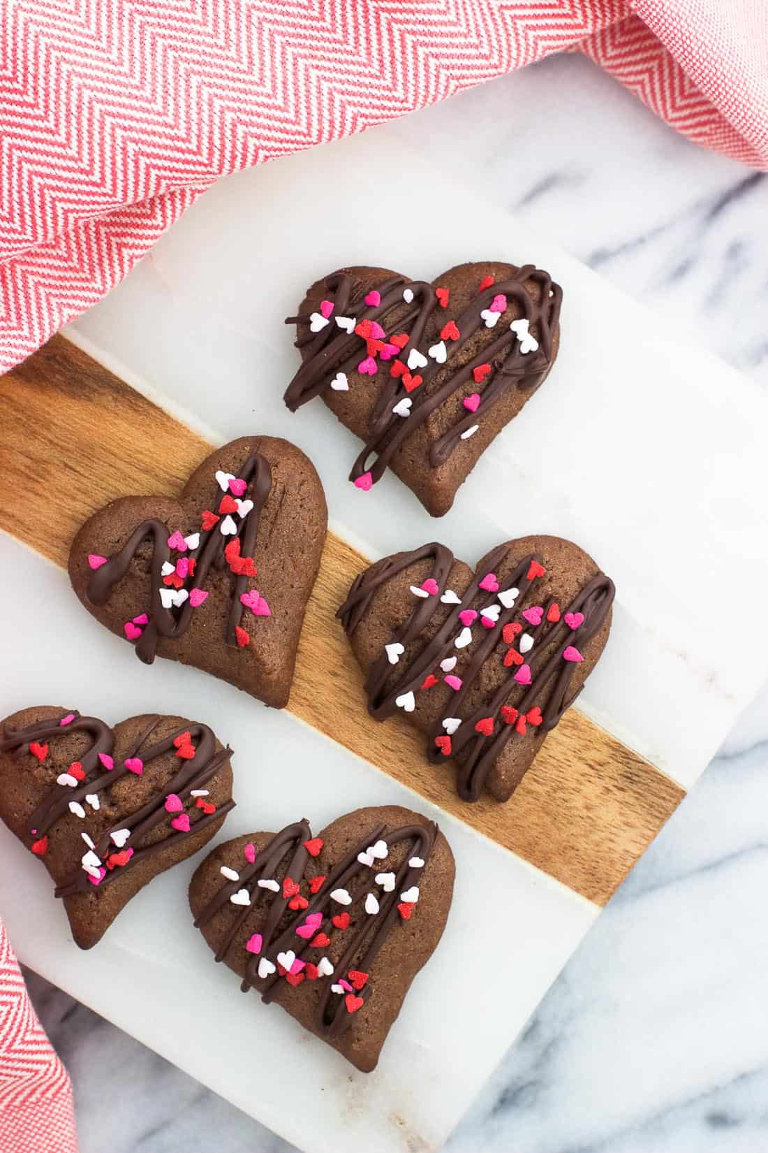 Heart-shaped spritz cookies on a marble board decorated with heart-shaped sprinkles