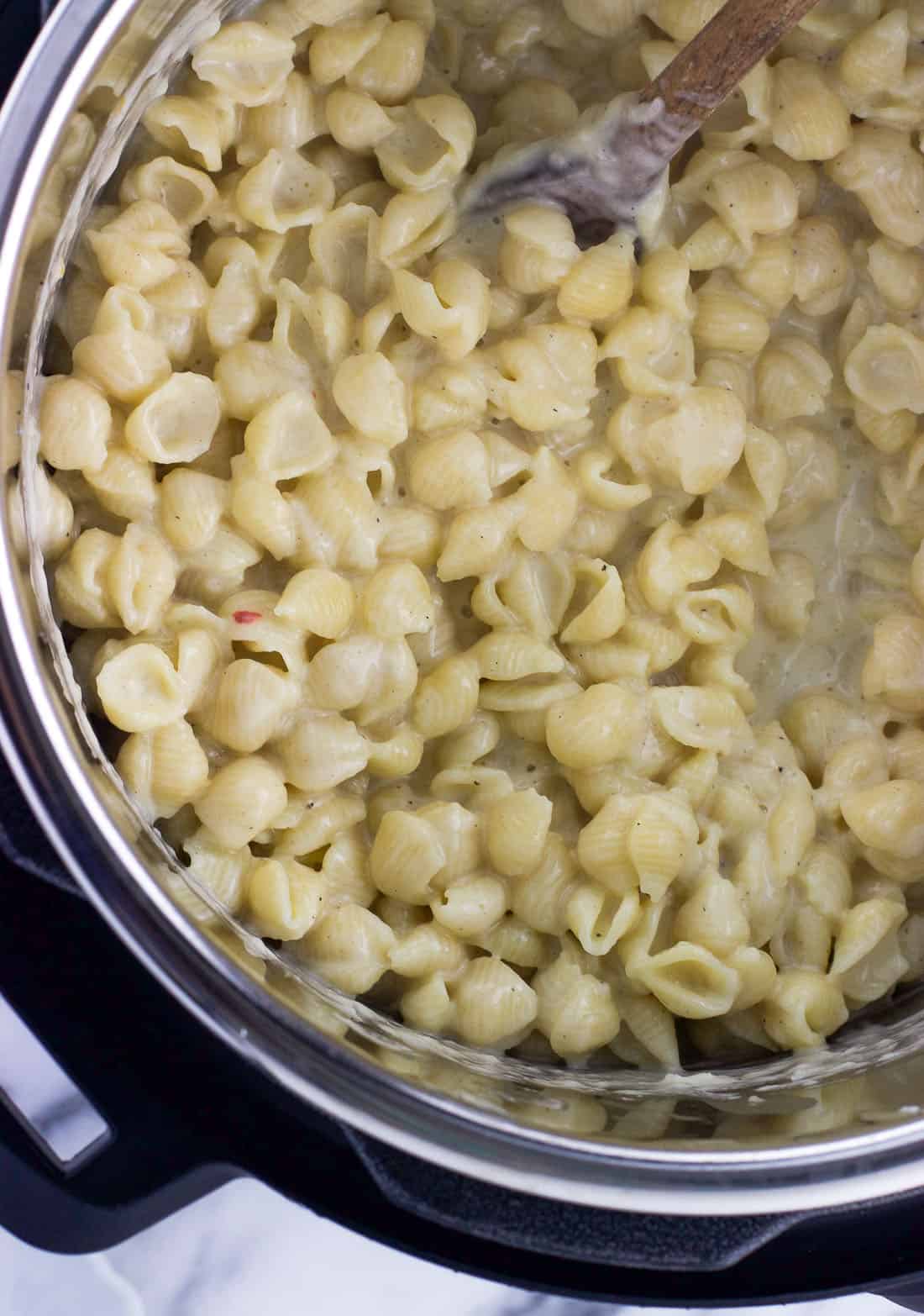 Creamy mac and cheese in the Instant Pot after stirring in the milk and cheese with a wooden spoon