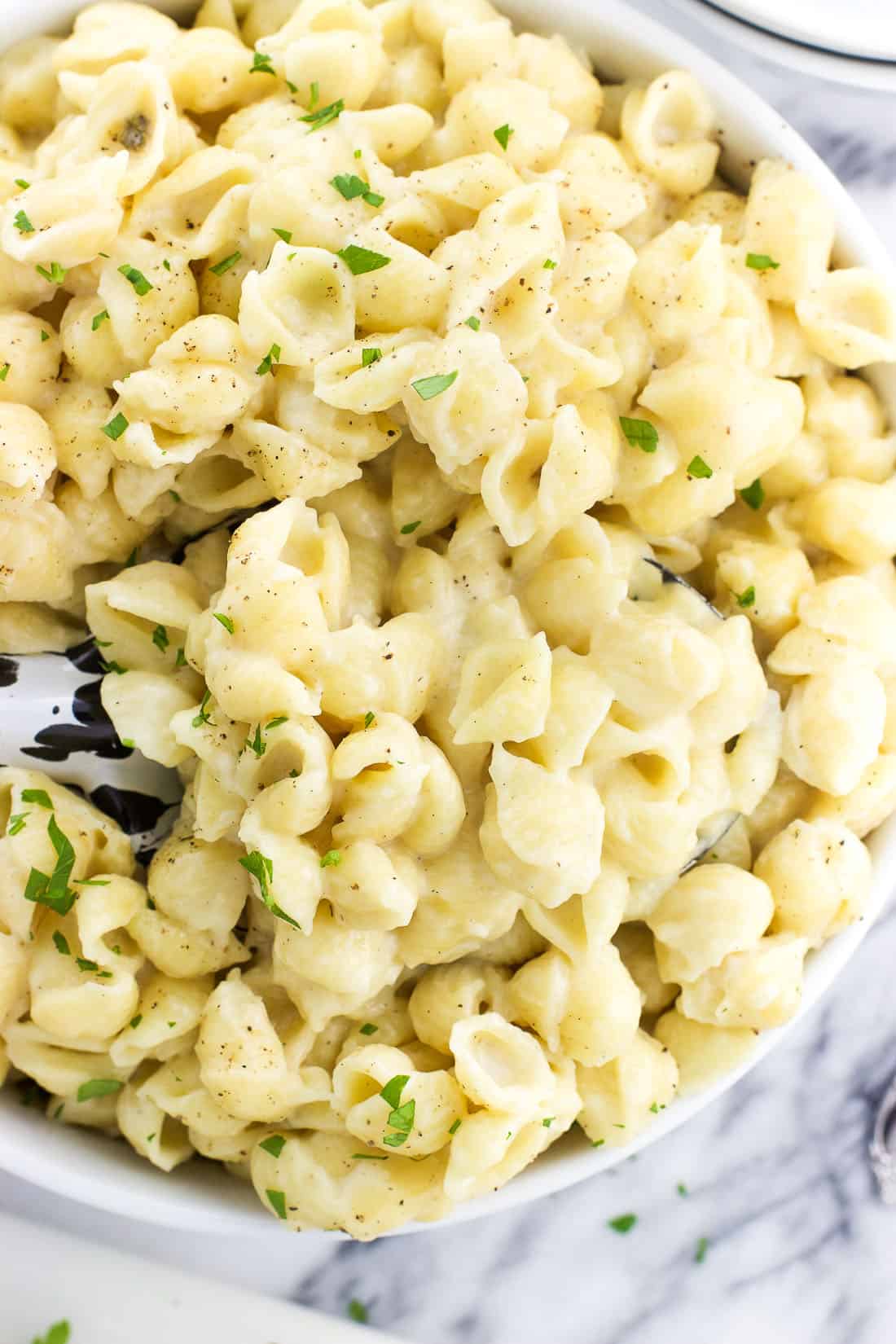 A serving spoon lifting out a spoonful from a bowl of mac and cheese.