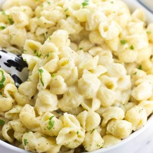 A serving bowl filled with mac and cheese with a serving spoon inserted