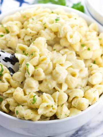 A serving bowl filled with mac and cheese with a serving spoon inserted