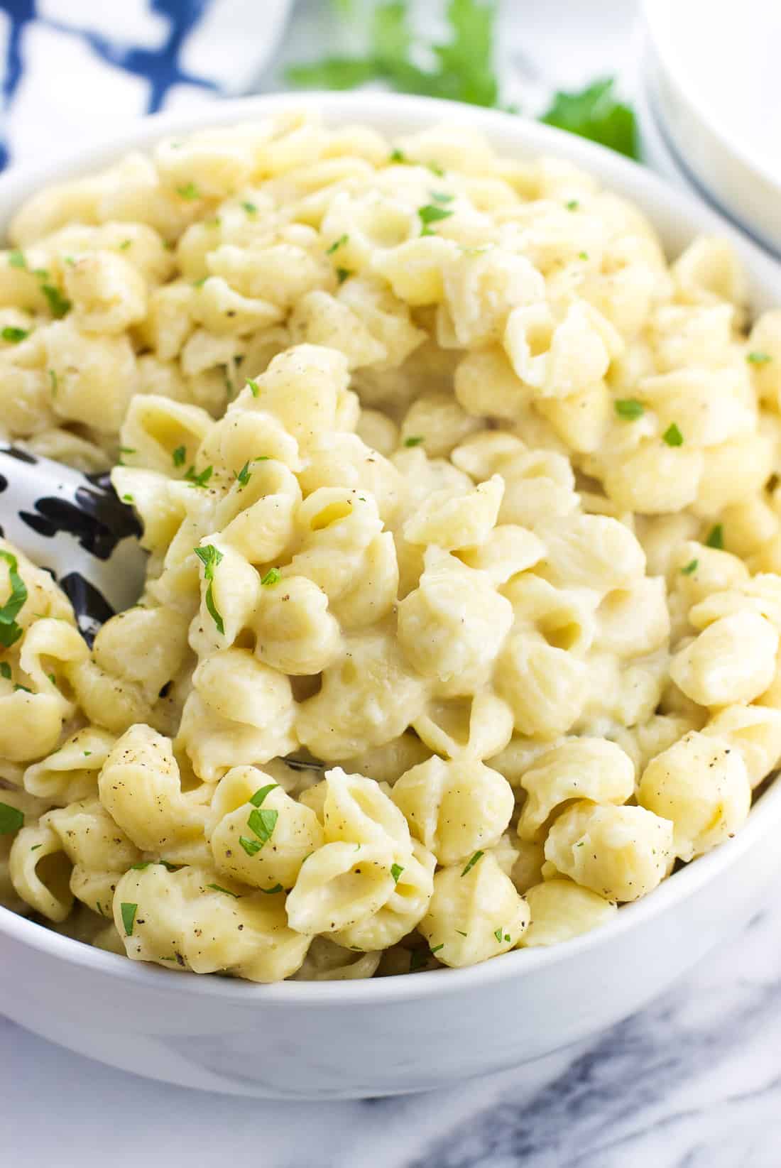 A ceramic serving bowl filled with mac and cheese with a serving spoon nestled in.