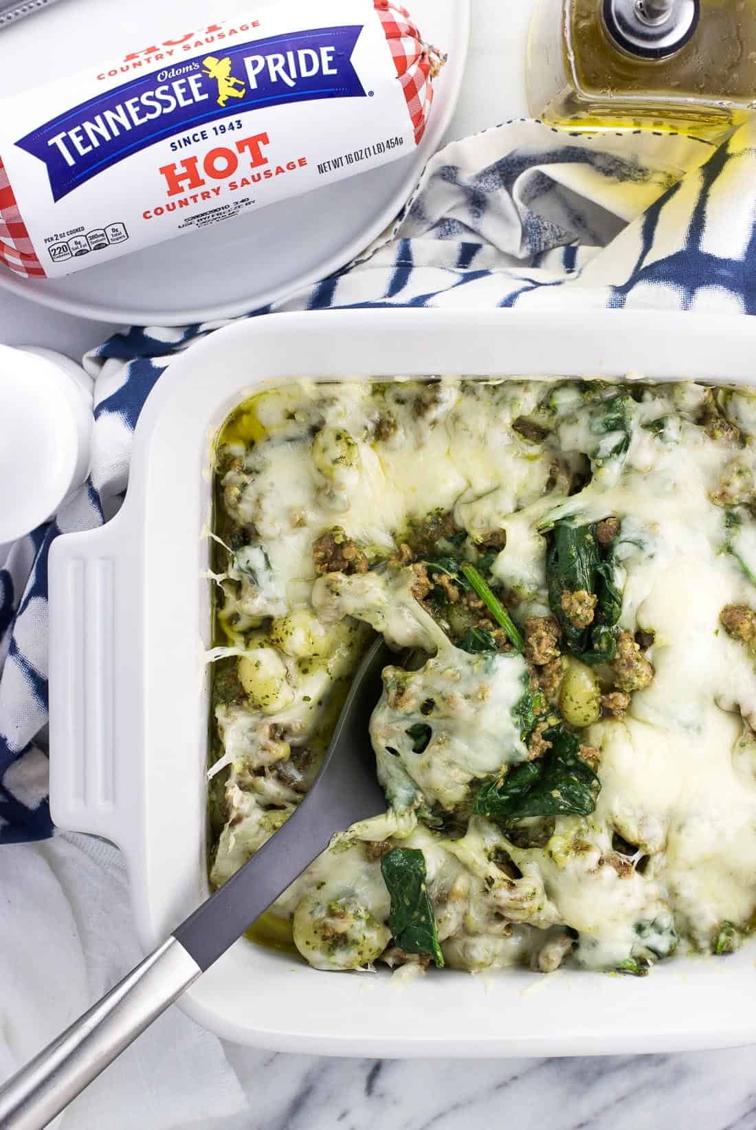 A serving spoon in a square dish of cooked pesto gnocchi bake.