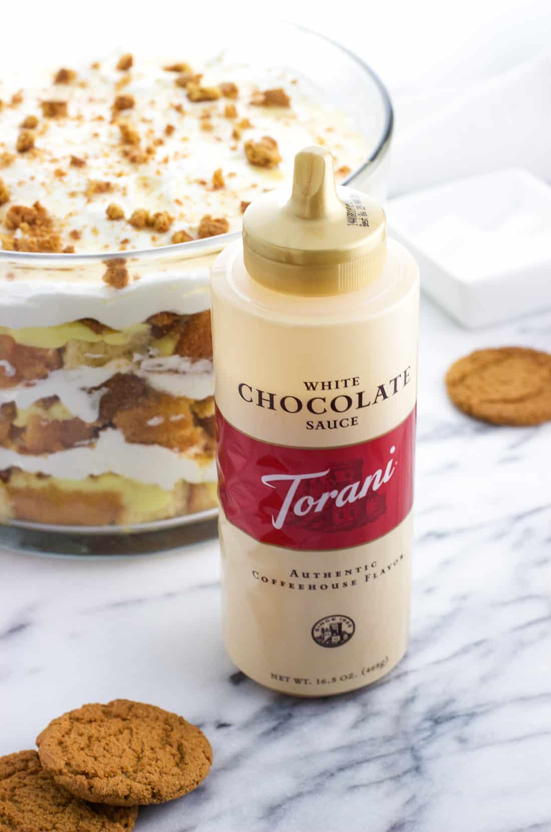 A close-up image of the Torani white chocolate sauce bottle in front of the trifle