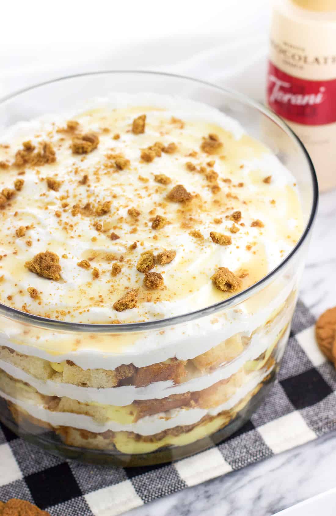 The pound cake trifle in a large trifle bowl with a bottle of Torani white chocolate syrup in the background