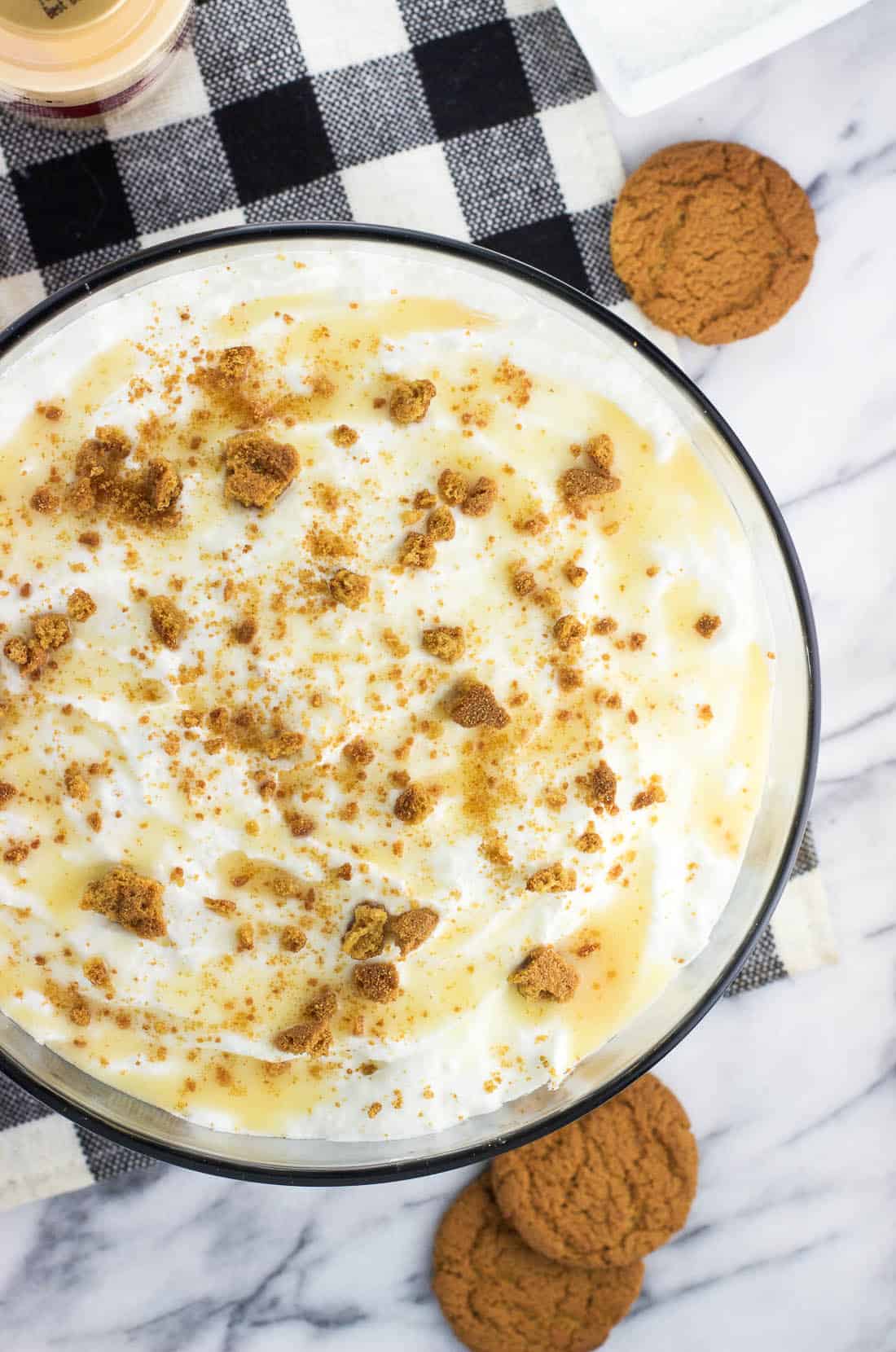 The pound cake trifle in a large bowl topped with whipped cream, white chocolate sauce, and crumbled gingersnap cookies