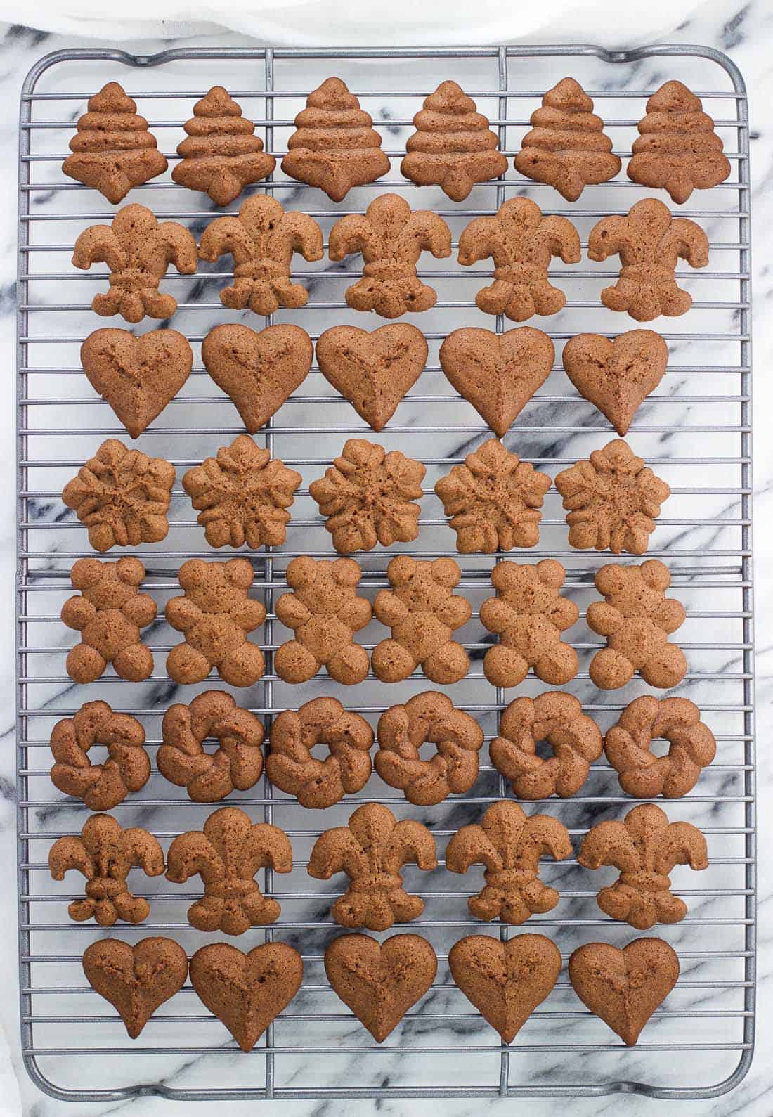 Rows of baked spritz cookies in different shapes on a wire cooling rack.