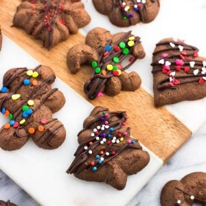 An assortment of chocolate spritz cookies drizzled with chocolate and sprinkles on a marble board.