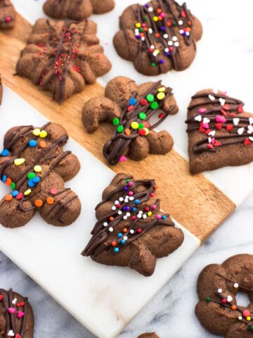 An assortment of chocolate spritz cookies drizzled with chocolate and sprinkles on a marble board.