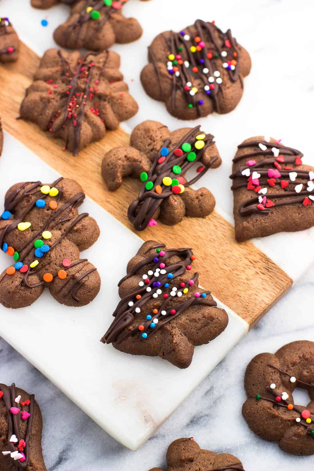An assortment of chocolate spritz cookies drizzled with chocolate and sprinkles on a marble board.